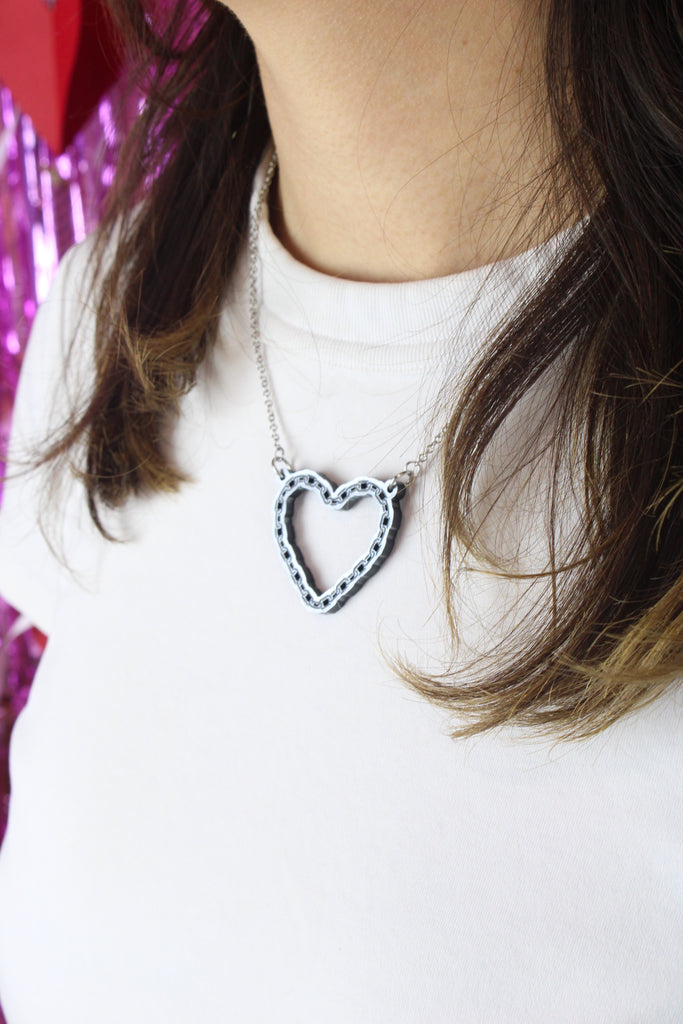 Model wearing a stainless steel chain with a cut out heart pendant with a chain style outline 