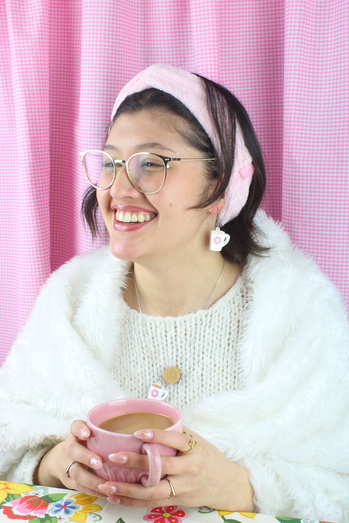 Model wearing Stainless steel chain with a chocolate digestive pendant reading 'Sour Cherry Digestive Biscuits' and a cup of tea pendant featuring a pink flower design. Model is also wearing the matching earrings. Model is also holding a cup of tea.