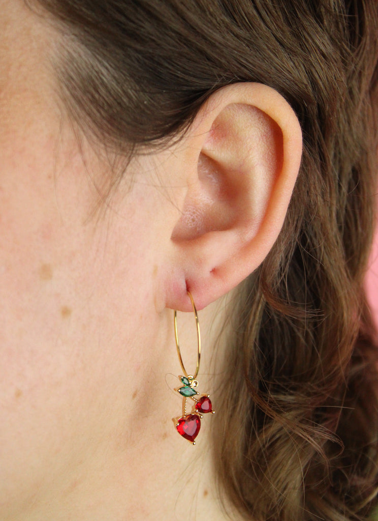 Ear wearing gold plated stainless steel hoops with glass cherry charms