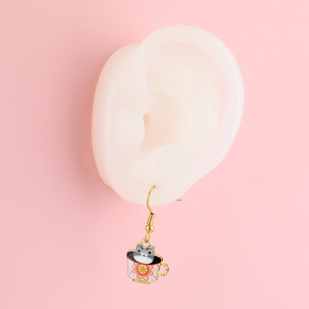 Ear wearing gold plated stainless steel earwires with charms featuring cats in a teacup