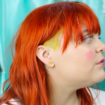 a woman with red hair wearing gold frog studs