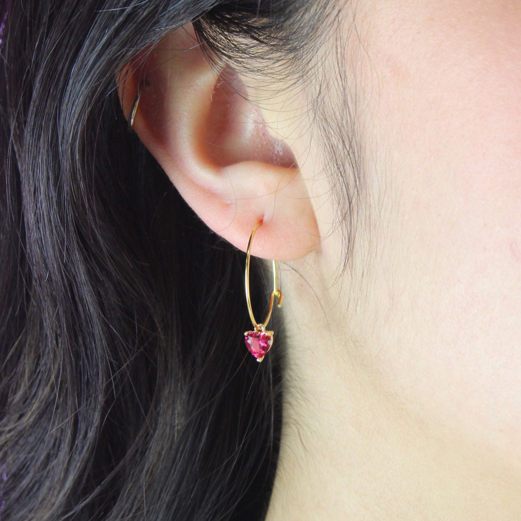 Model wearing gold plated stainless steel hoop with a red glass-effect heart charm