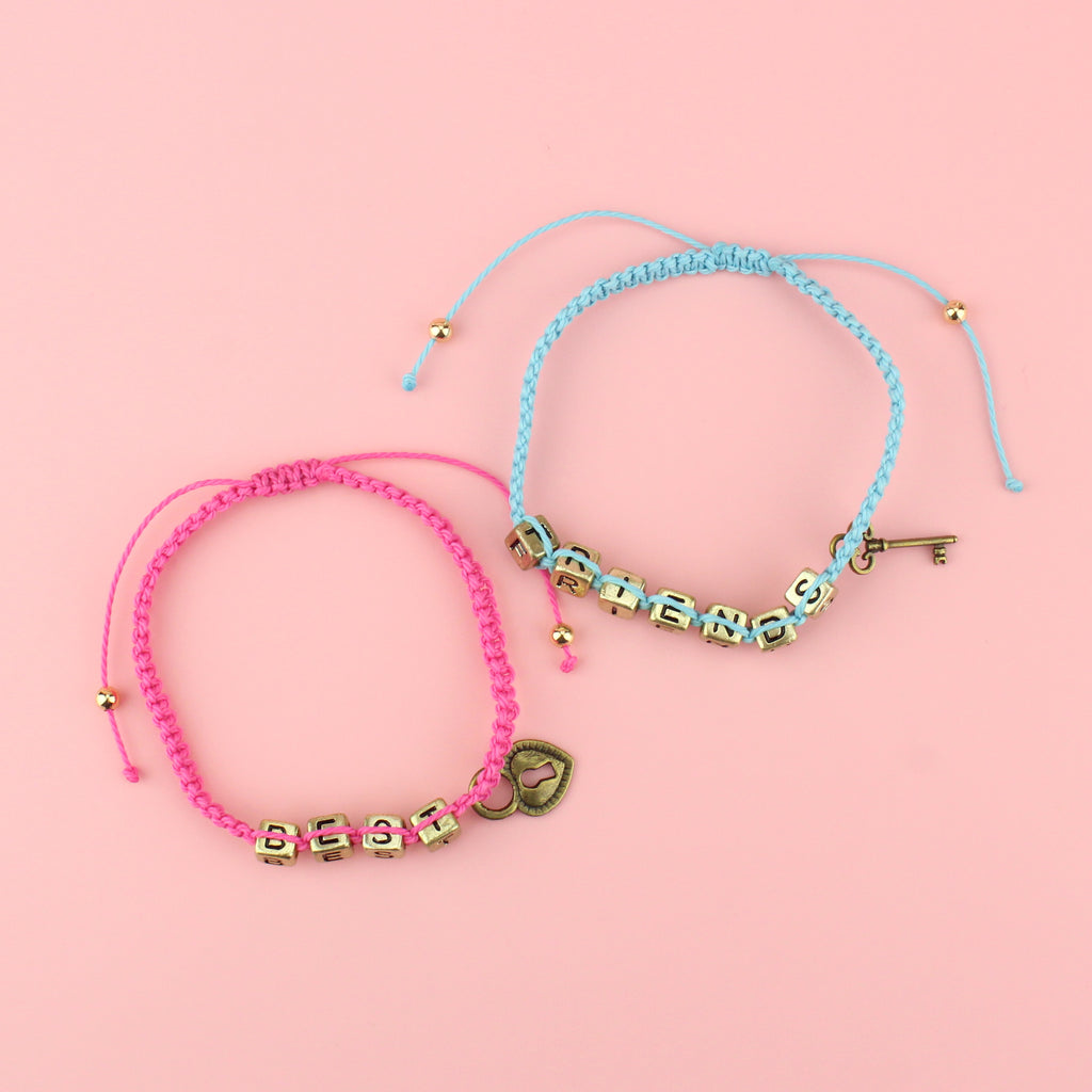 Pink and blue waxed cord braided bead bracelets. With gold plated base metal charms reading 'Best' on the pink bracelet with a heart locket and 'Friends' on the blue with a key