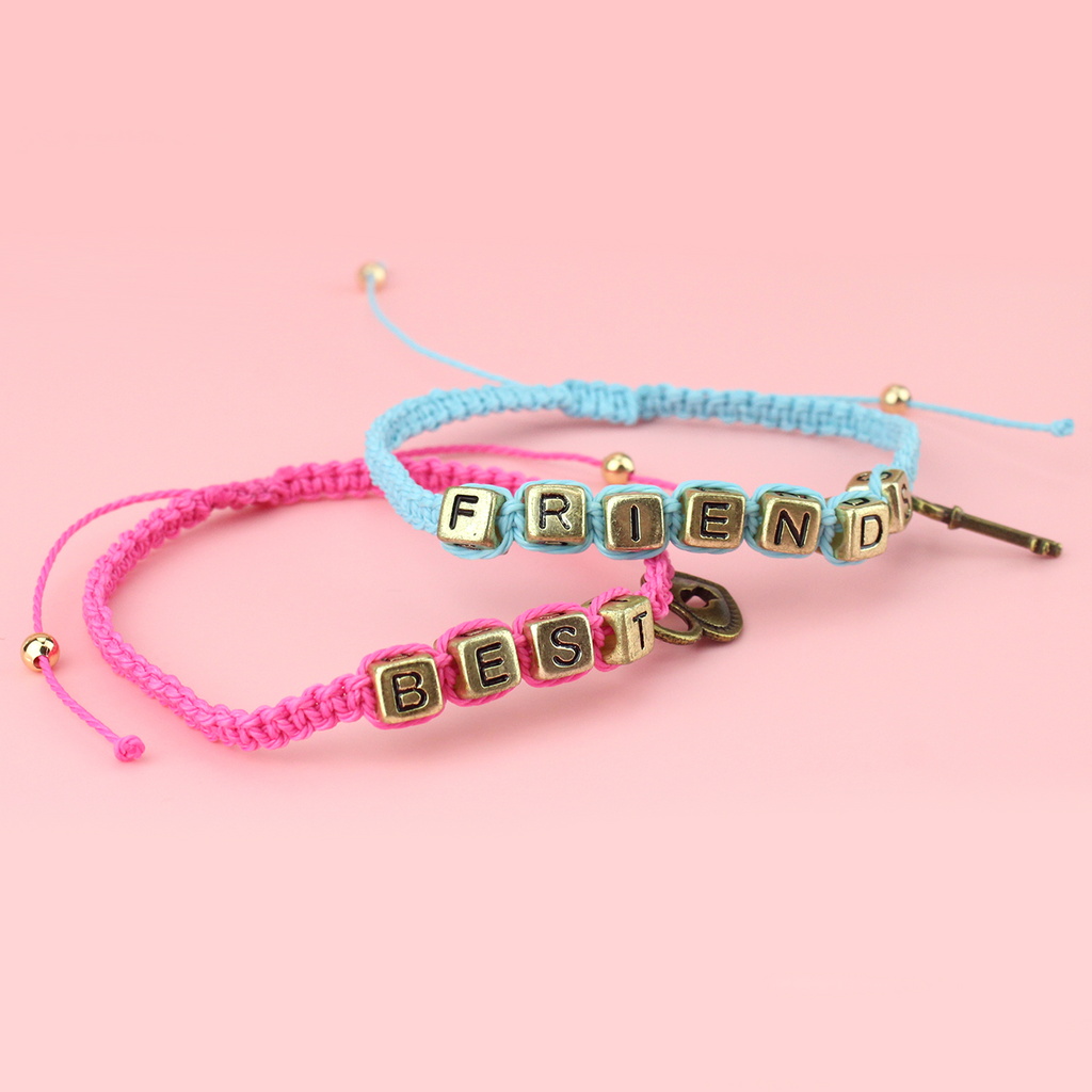 Pink and blue waxed cord braided bead bracelets. With gold plated base metal charms reading 'Best' on the pink bracelet with a heart locket and 'Friends' on the blue with a key