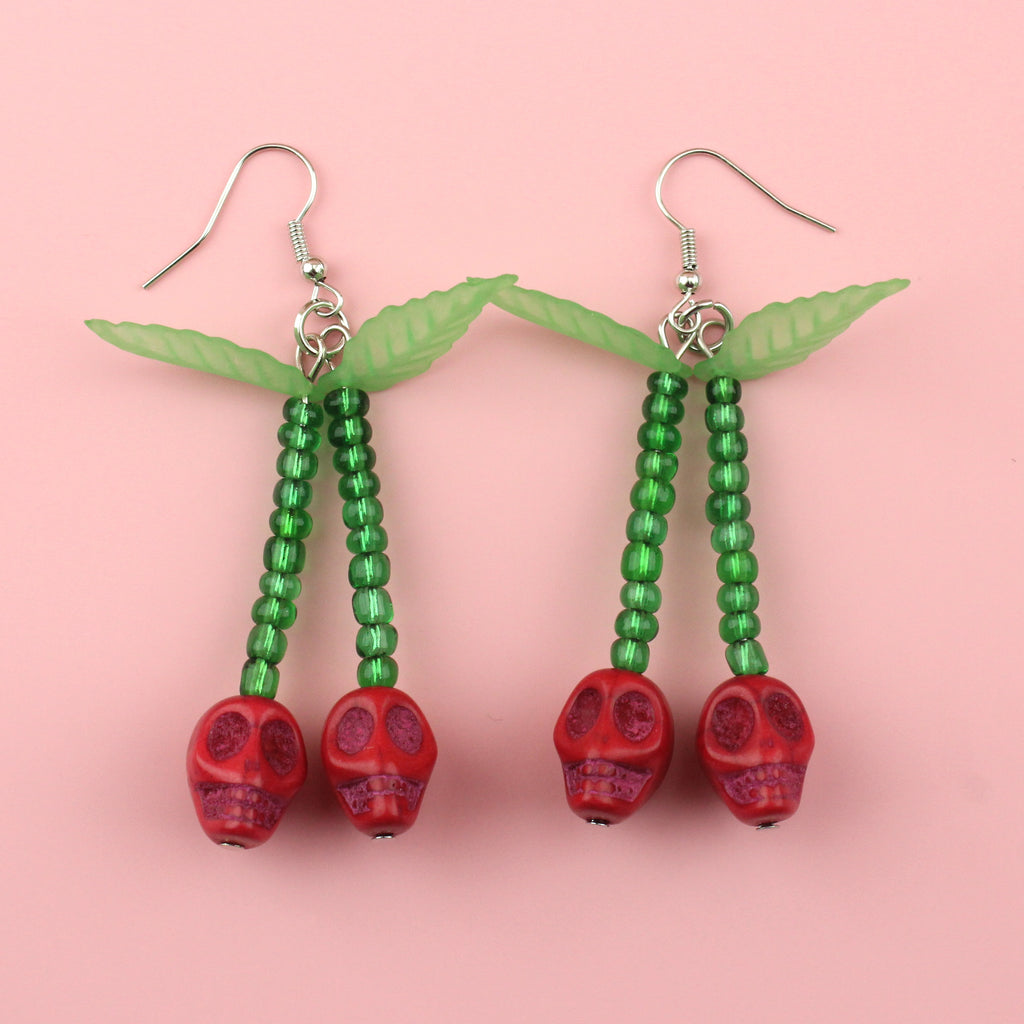 Red skull cherry charms on stems made out of green beads with two leaves attached at the top on stainless steel earwires
