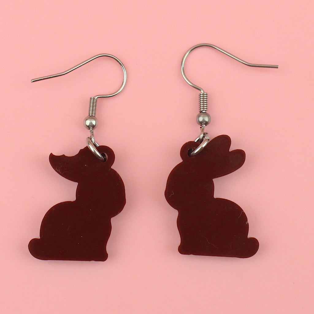 Showing back of charms in the shape of chocolate bunnies with a bite taken out of one ear on stainless steel