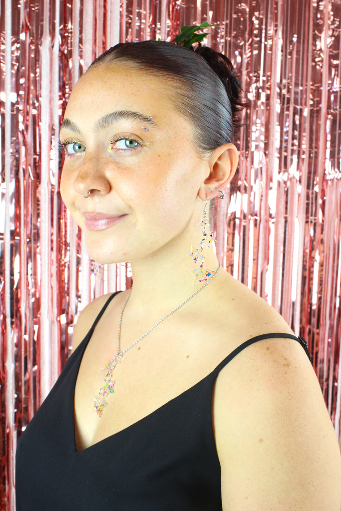 Model wearing four confetti star charms hung from stainless steel earwires ranging in size with a small star at the top followed by two medium stars and a large star at the bottom