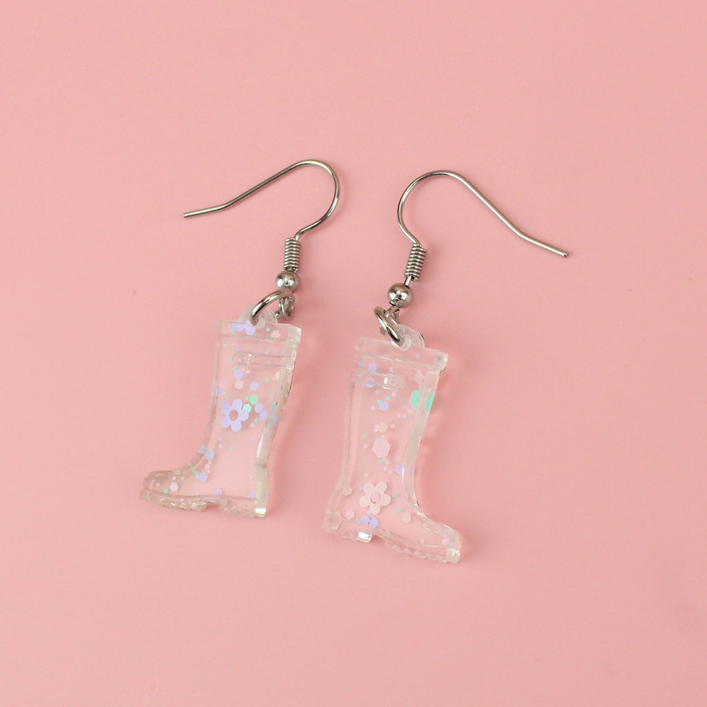 Transparent wellie boot charms with pieces of confetti and pastel flowers inside on stainless steel earwires