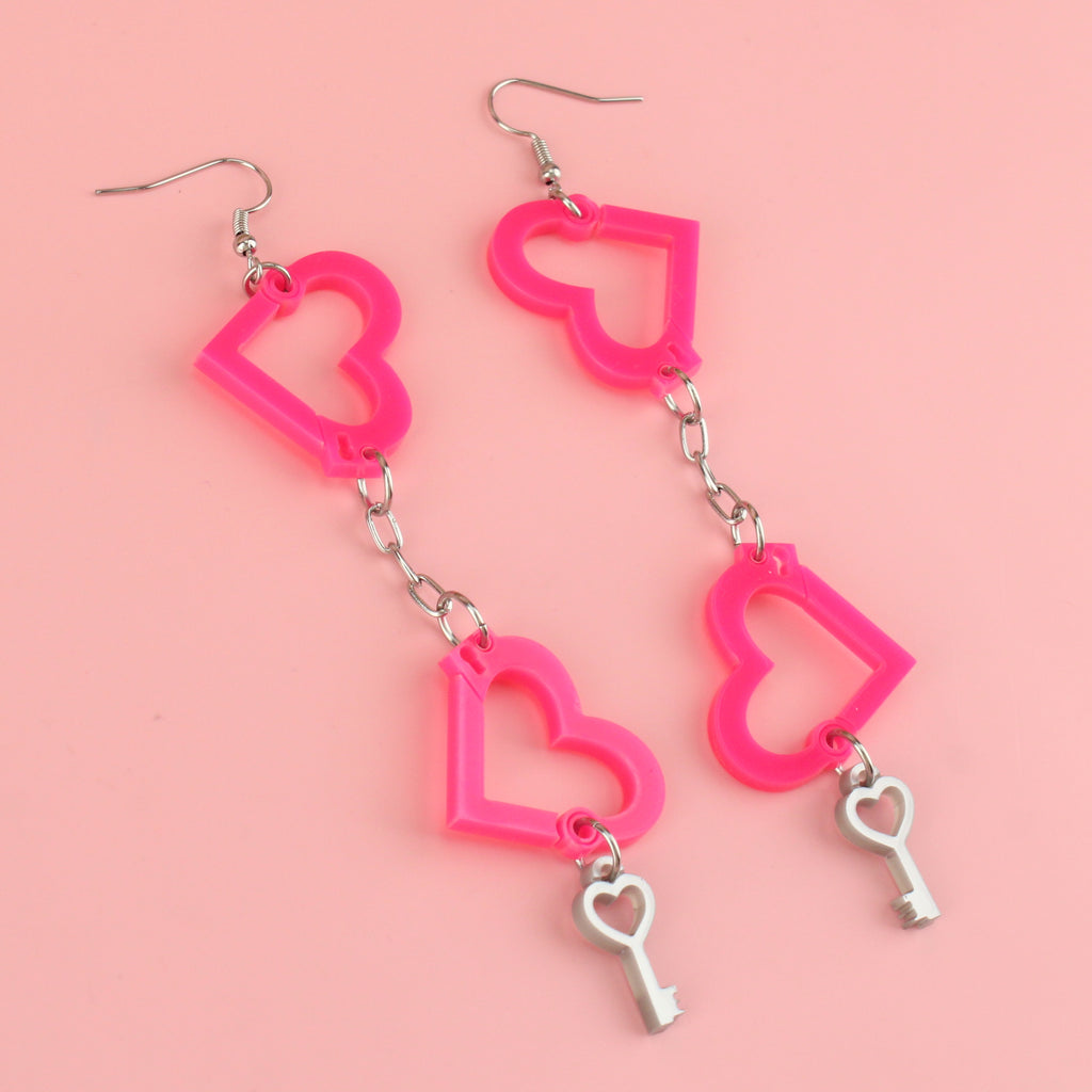 neon pink acrylic heart charms chained together to resemble handcuffs, with a key charm attached to the bottom