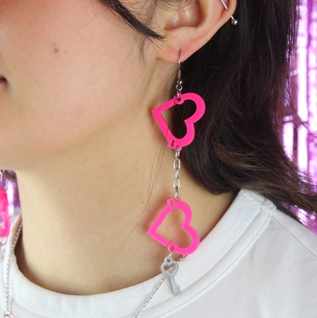 model wearing neon pink acrylic heart charms chained together to resemble handcuffs, with a key charm attached to the bottom