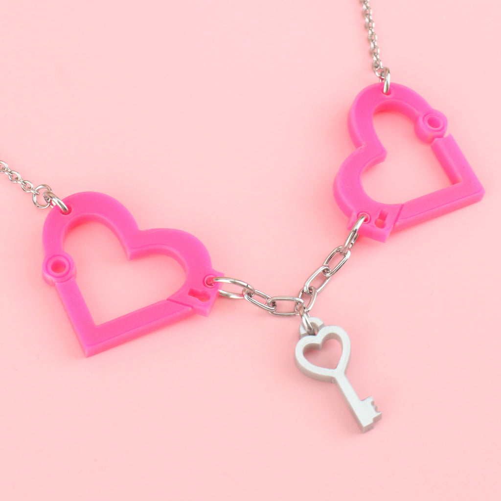 neon pink acrylic heart charms chained together to resemble handcuffs, with a key charm in the middle of the two handcuff pendants, on a stainless steel chain