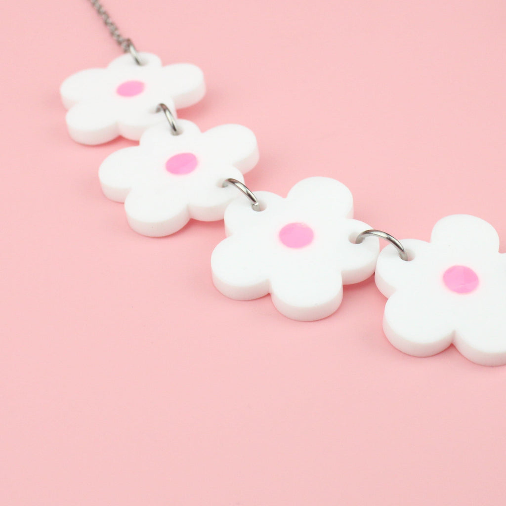 Close up of white perspex flowers with a pink glow in the dark centre on a stainless steel chain