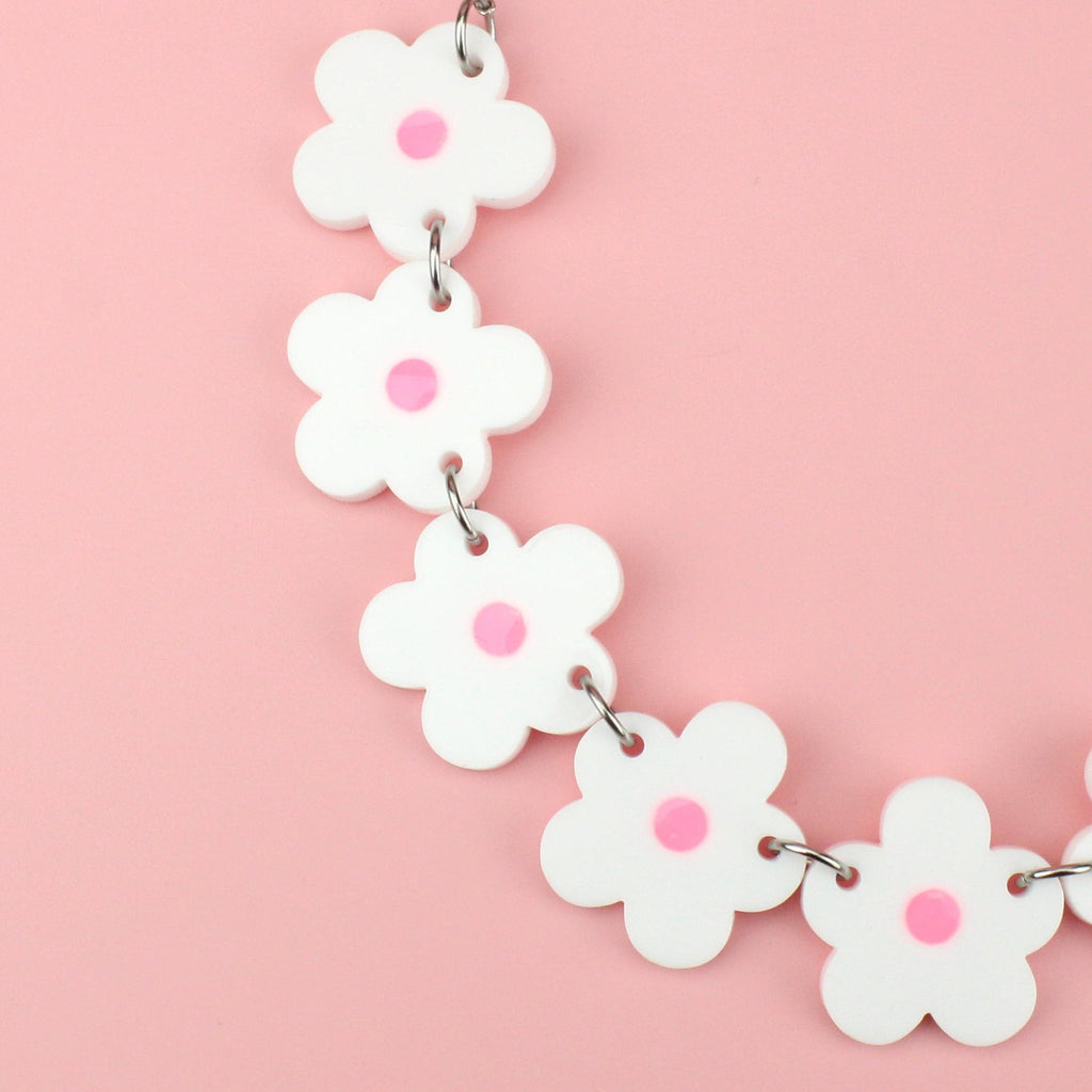 Close up of white perspex flowers with a pink glow in the dark centre on a stainless steel chain