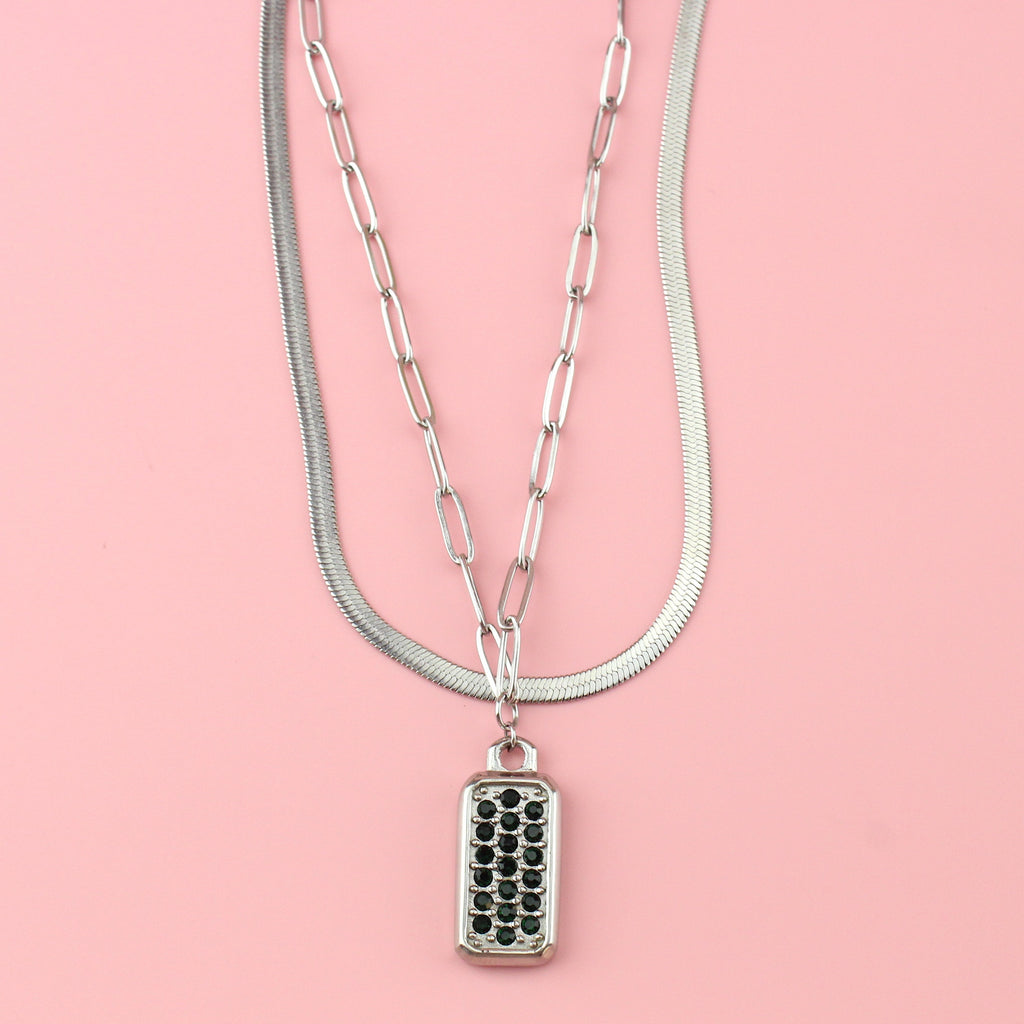 A layered necklace featuring both an oval link and snake chain with a rectangular pendant with emerald cubic zirconia stones