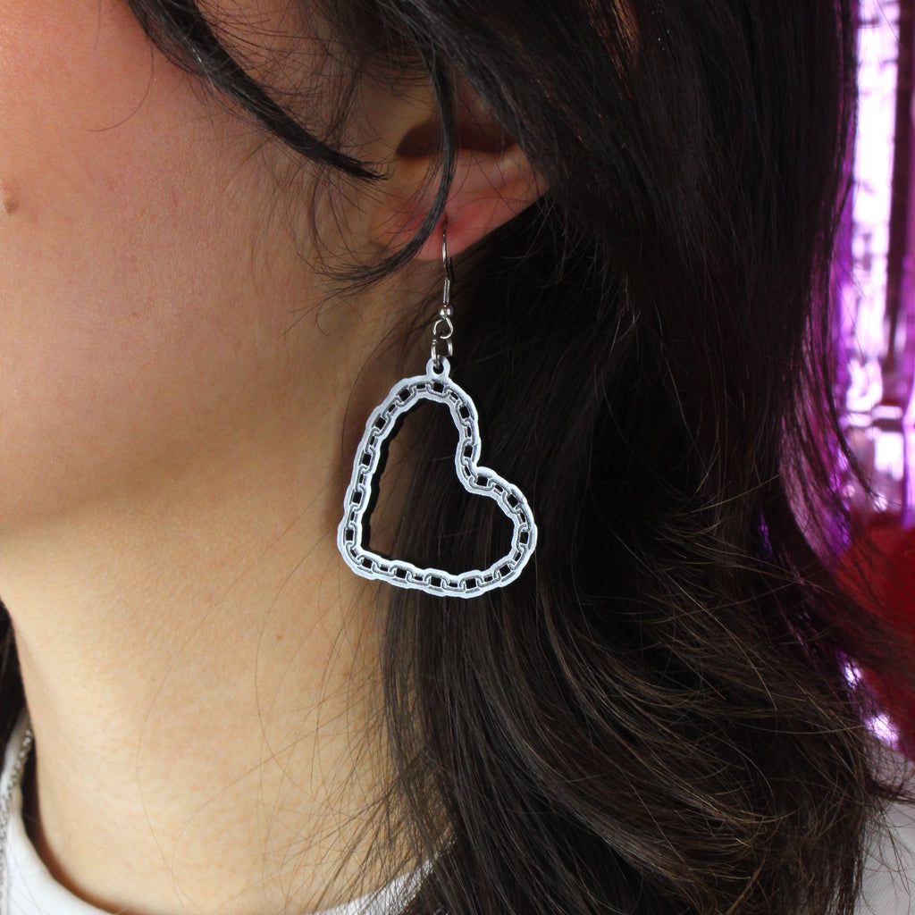 Model wearing acrylic cut out heart charms with a chain-style outline on stainless steel earwires