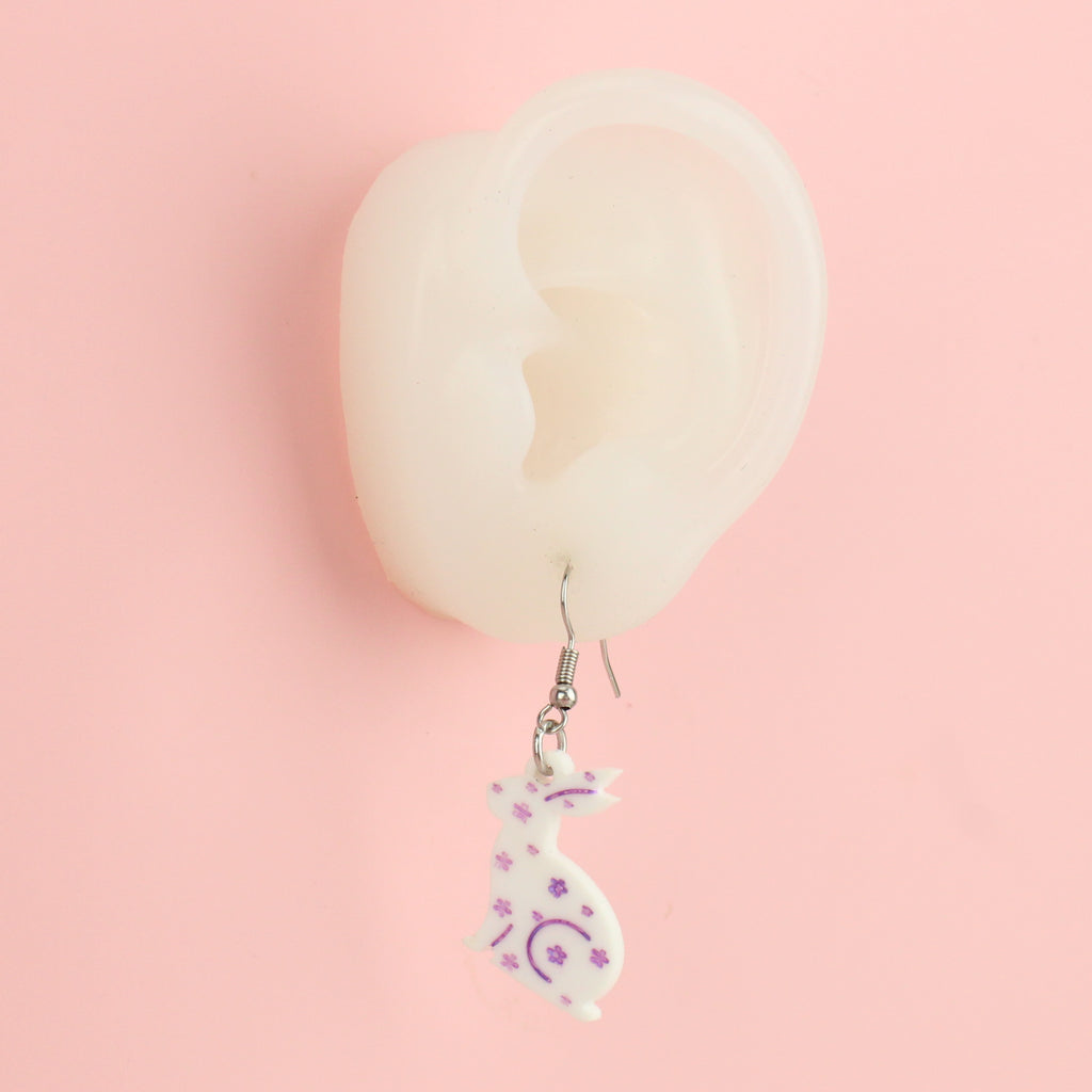 Ear wearing white acrylic bunnies with hand-painted purple flowers on stainless steel earwires