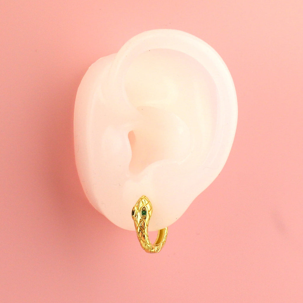 Ear wearing gold plated snake hoop earrings featuring green cubic zirconia eyes