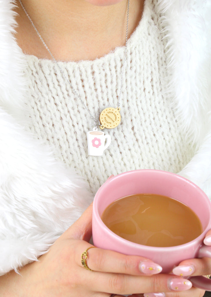 Model wearing Stainless steel chain with a chocolate digestive pendant reading 'Sour Cherry Digestive Biscuits' and a cup of tea pendant featuring a pink flower design. Model is also holding a cup of tea.