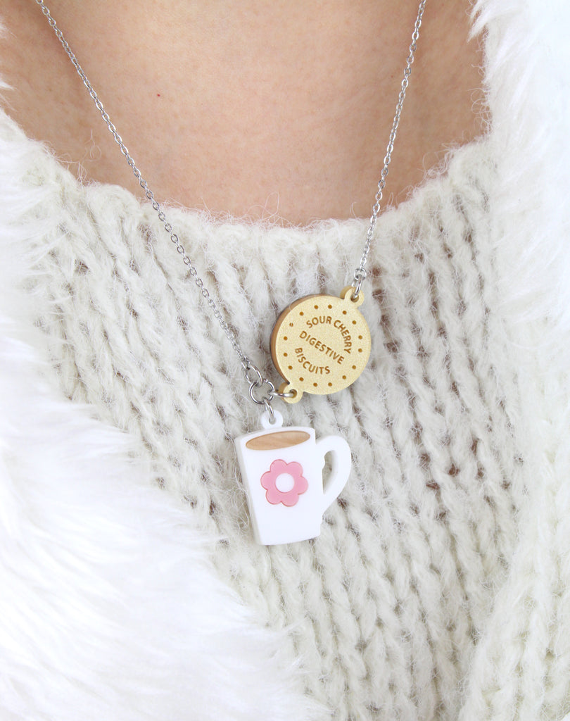 Model wearing Stainless steel chain with a chocolate digestive pendant reading 'Sour Cherry Digestive Biscuits' and a cup of tea pendant featuring a pink flower design