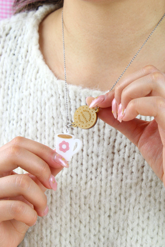 Model wearing Stainless steel chain with a chocolate digestive pendant reading 'Sour Cherry Digestive Biscuits' and a cup of tea pendant featuring a pink flower design