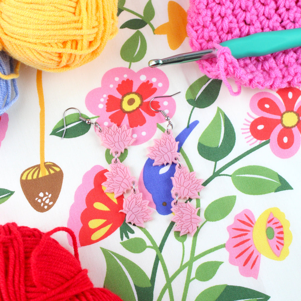 Pink acrylic cascading lotus flower charms on stainless steel earwires. Shown on a table with yarn.