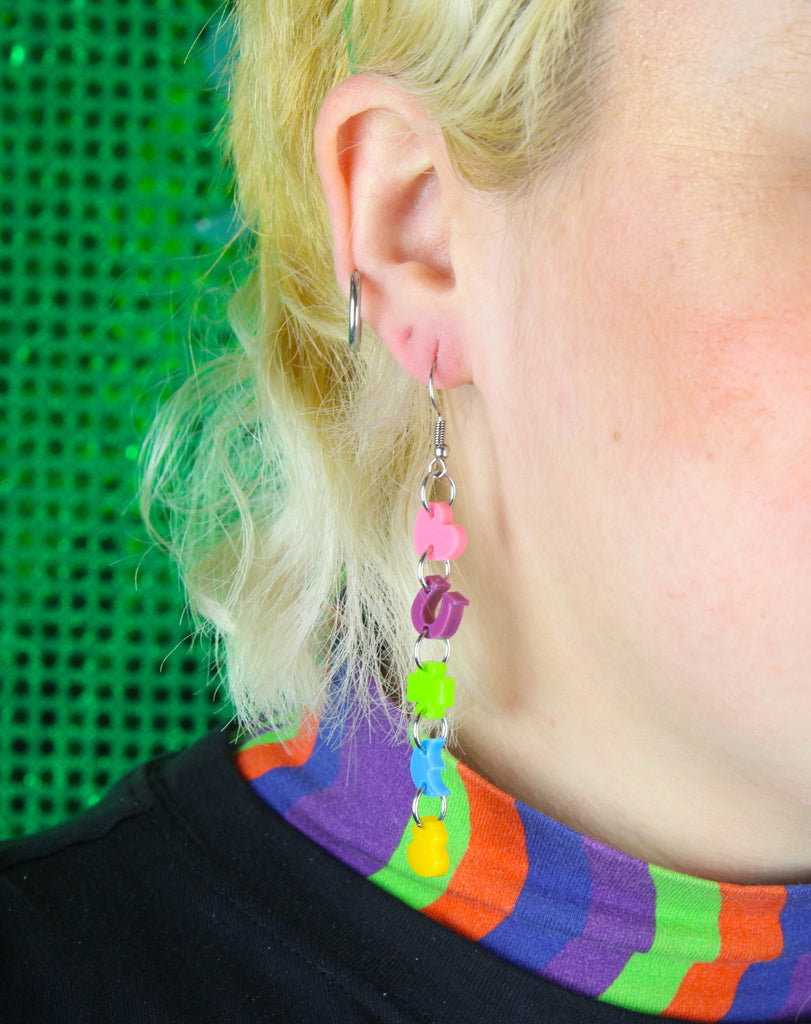 Model wearing A chain of lucky charms featuring a pink heart, a purple horseshoe. a green four leaf clover, a blue moon and orange pot of gold on stainless steel earwires