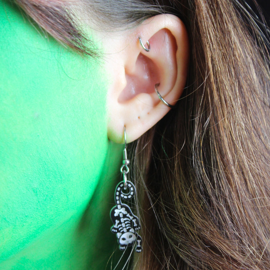 Model wearing cat skeleton charms on stainless steel earwires 