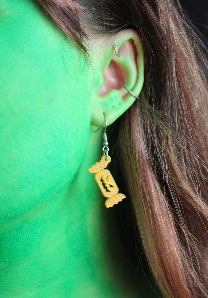 Ear wearing Orange sweet wrapper charms with carved faces on stainless steel earwires