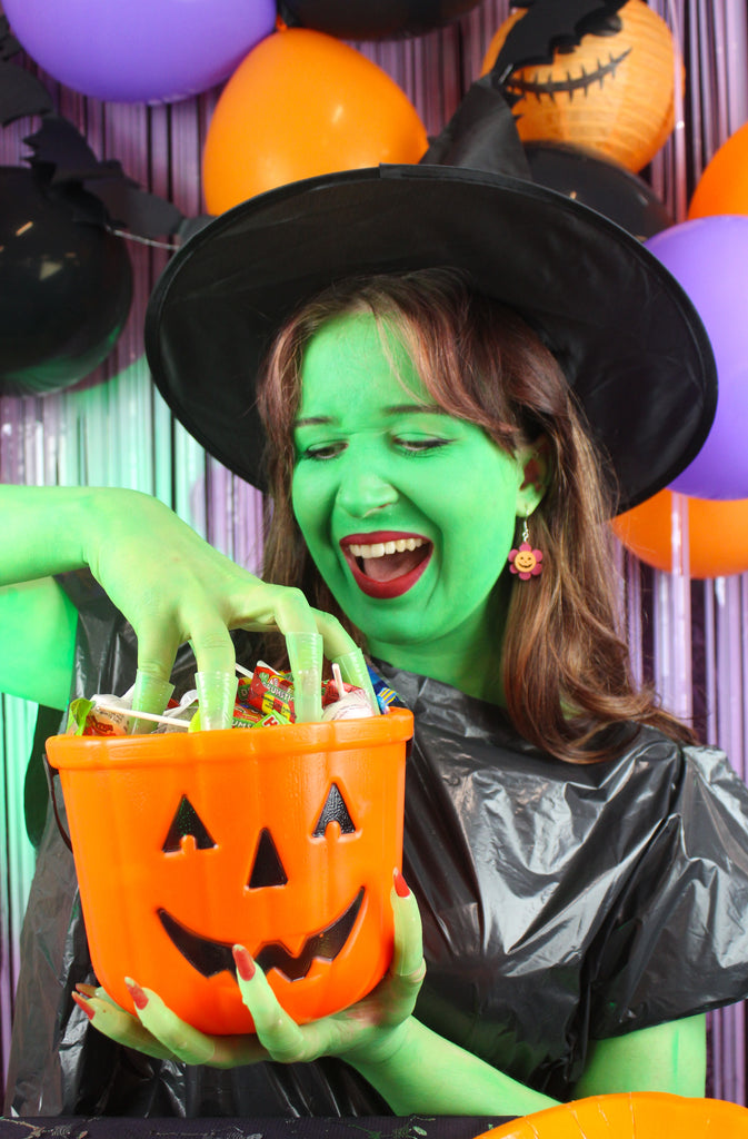 Model wearing pink flower charm with pumpkin face in the middle on stainless steel earwires