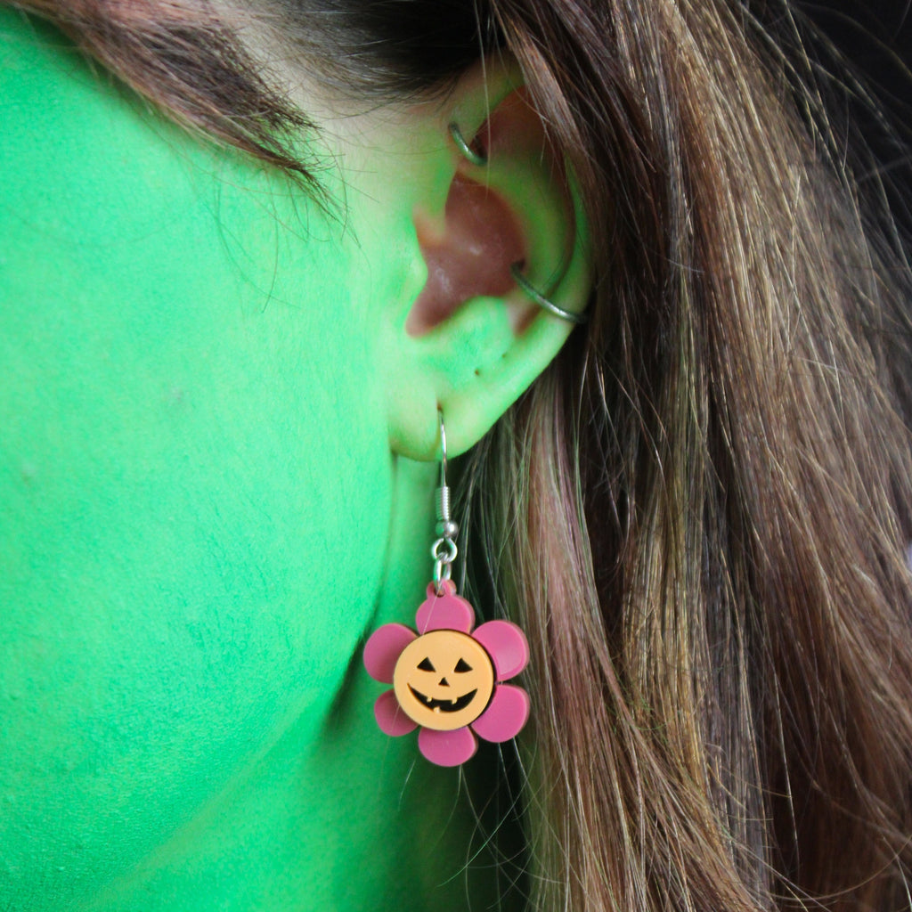 Model wearing pink flower charm with pumpkin face in the middle on stainless steel earwires