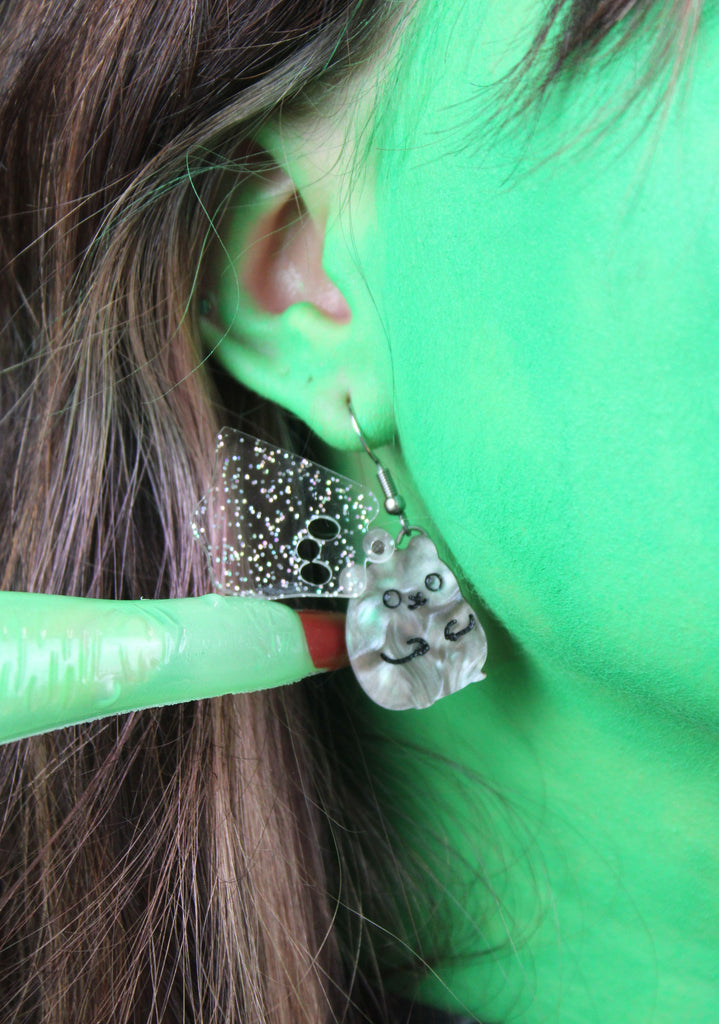 Ear wearing Grey hamster charms with an additional layer of holographic glitter to replicate a ghost on stainless steel earwires