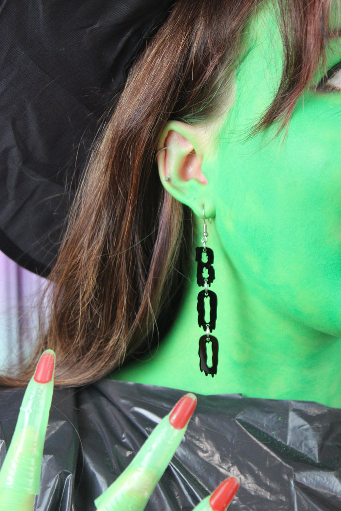 MODEL WEARING THE LETTERS B, O, O SPELLED OUT VERTICALLY WITH A BLACK DRIPPY EFFECT ON STAINLESS STEEL EARWIRES