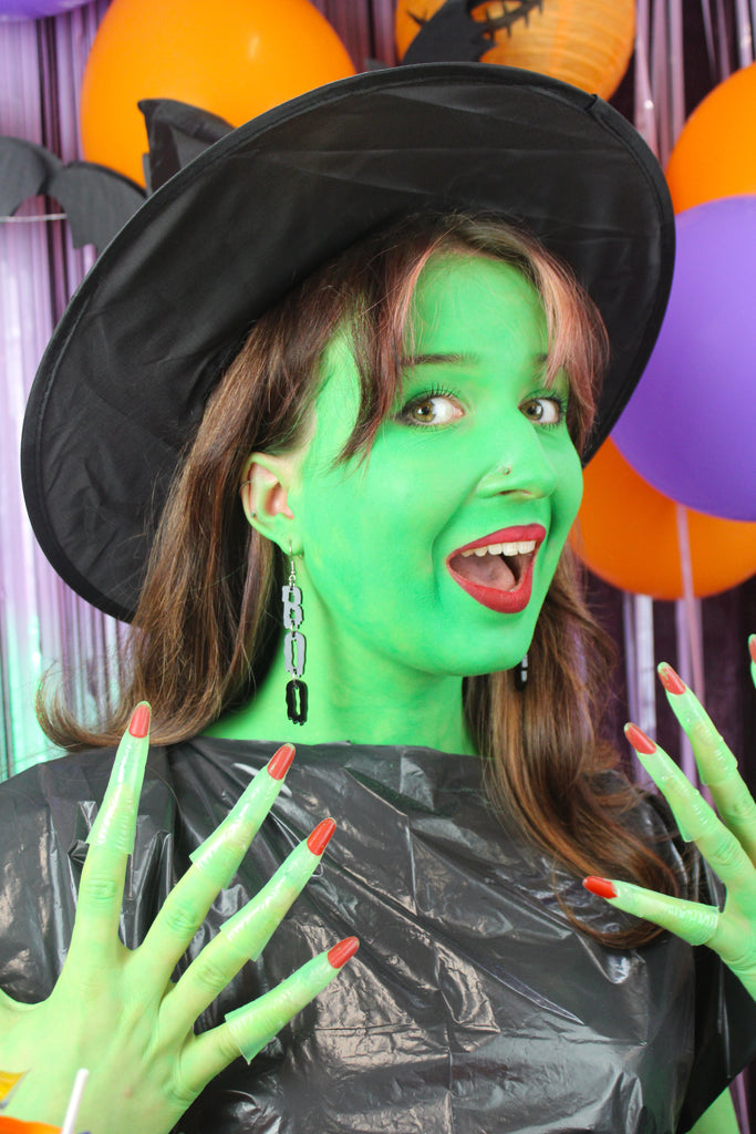 MODEL WEARING THE LETTERS B, O, O SPELLED OUT VERTICALLY WITH A BLACK DRIPPY EFFECT ON STAINLESS STEEL EARWIRES