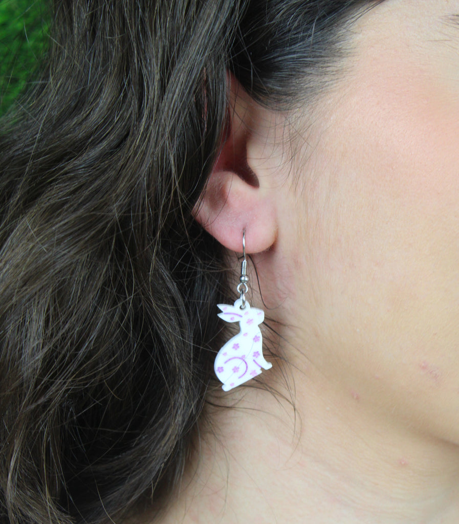 Model wearing white acrylic bunnies with hand-painted purple flowers on stainless steel earwires