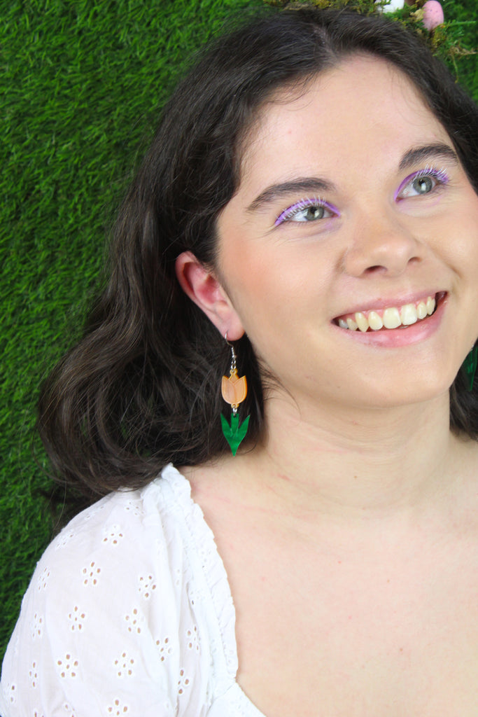 Model wearing orange tulip charms with green stems on stainless steel earwires