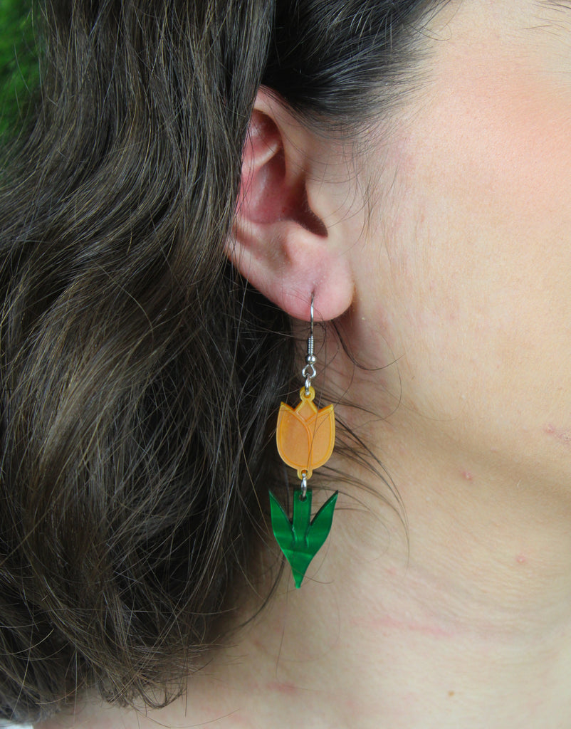 Model wearing orange tulip charms with green stems on stainless steel earwires
