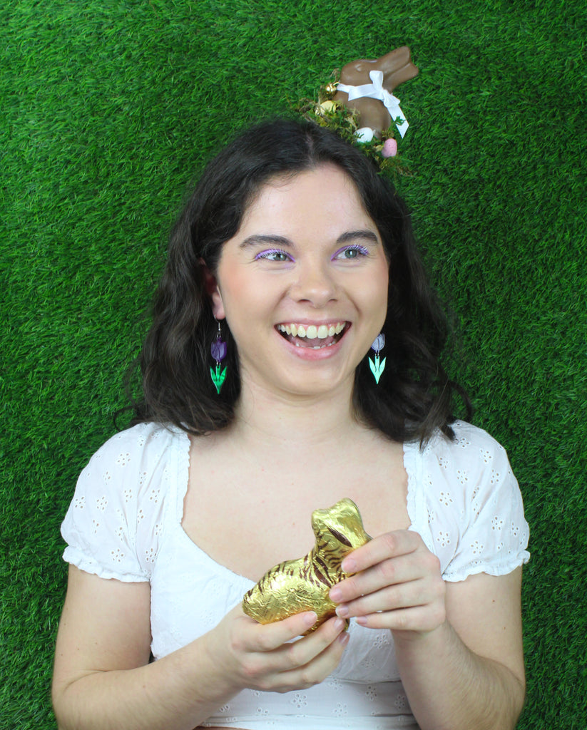 Model wearing Purple acrylic tulip charms with green stems on stainless steel earwires. Model is also holding a chocolate bunny.