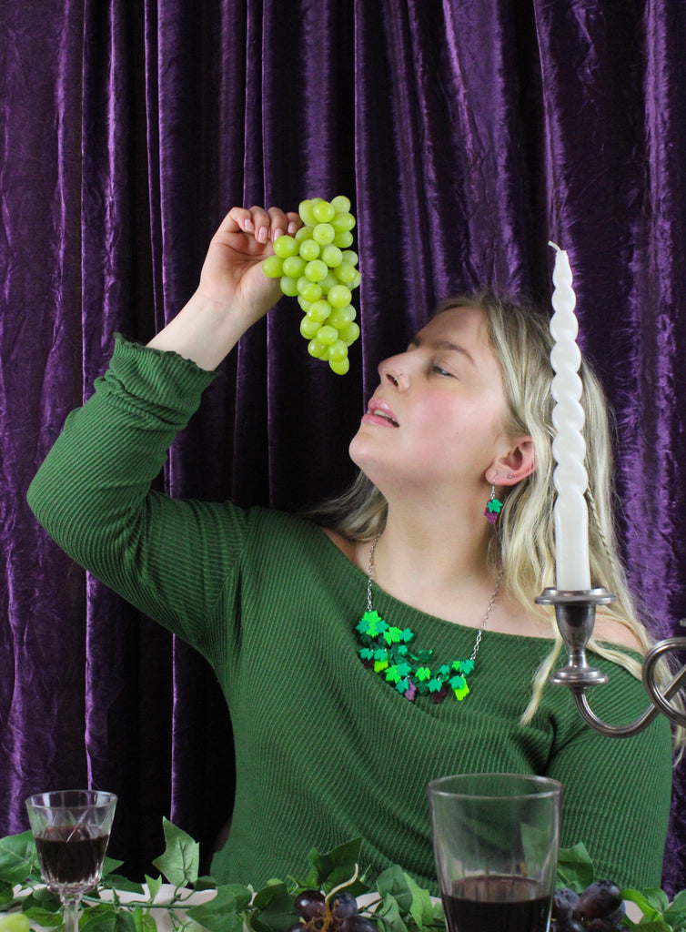 Model wearing arcrylic earrings featuring a bunch of purple grapes and the stem