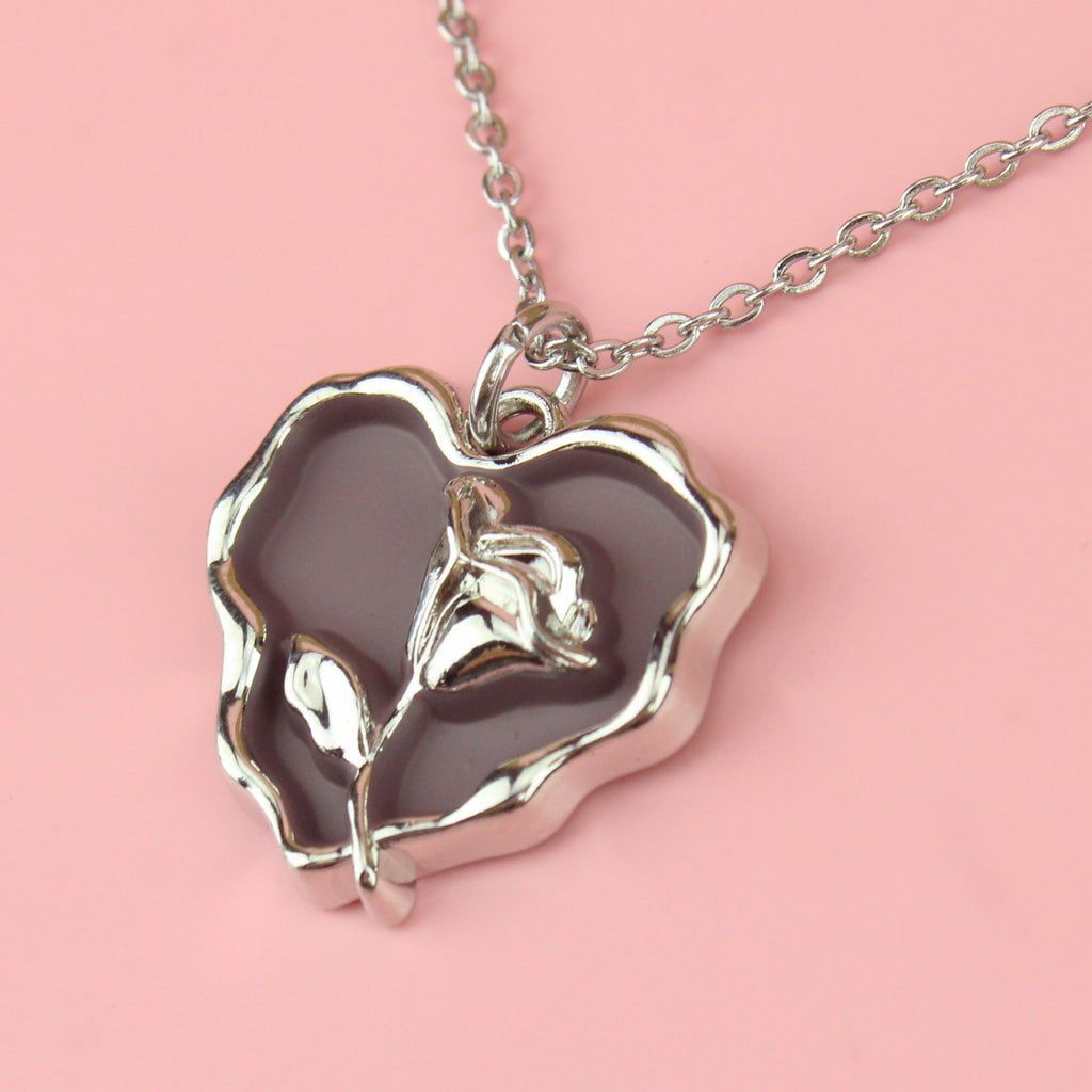 a base metal pendant with a beautiful rose in the centre of a purple heart, suspended from sleek stainless steel chains