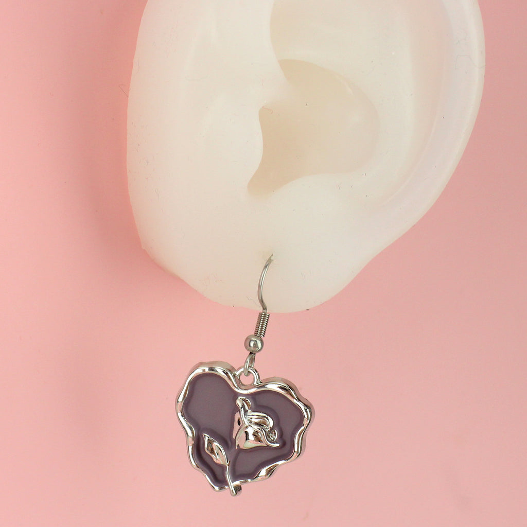 Ear wearing a base metal charm with a beautiful rose in the centre of a purple heart, suspended from sleek stainless steel ear wires