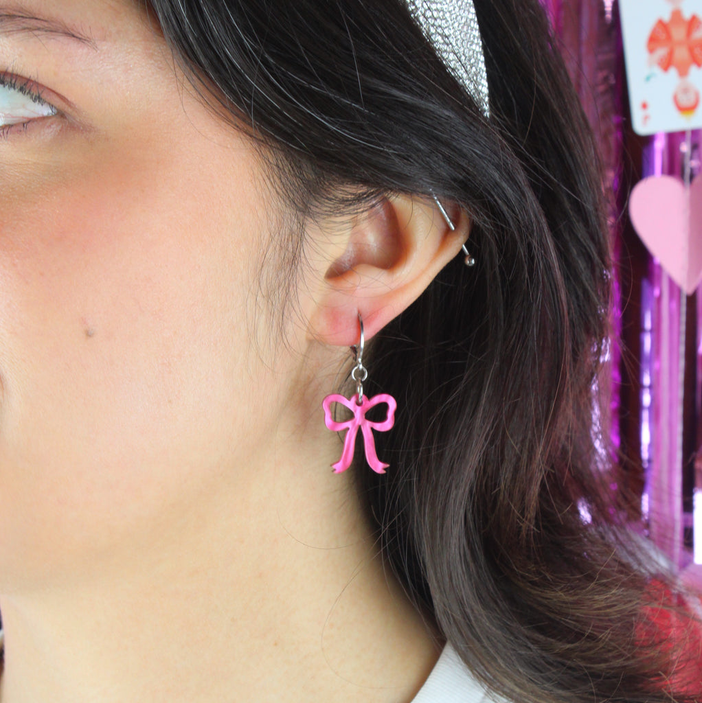 Model wearing Mini pink marble bow charms on stainless steel huggie hoops
