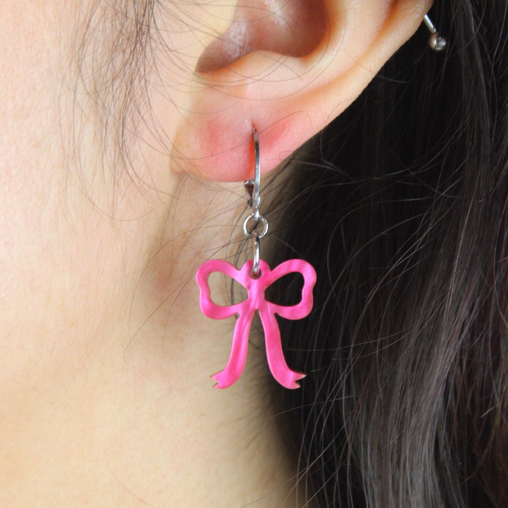 Model wearing Mini pink marble bow charms on stainless steel huggie hoops