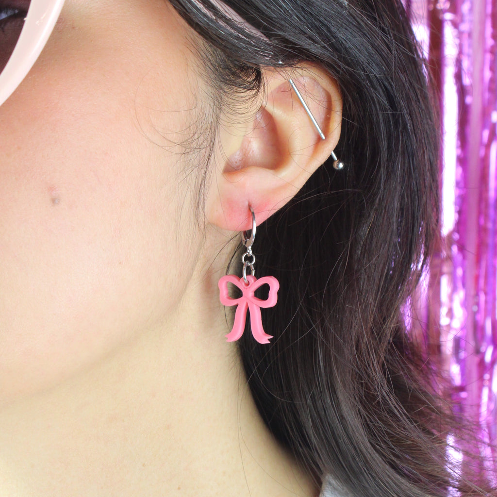 Model wearing mini rose pink bow charms on stainless steel huggie hoops