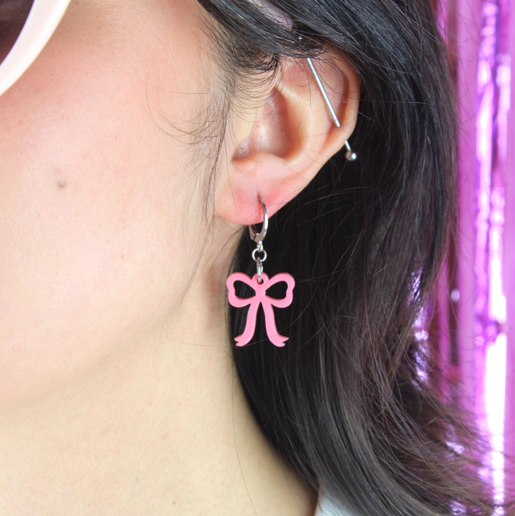 Model wearing mini rose pink bow charms on stainless steel huggie hoops
