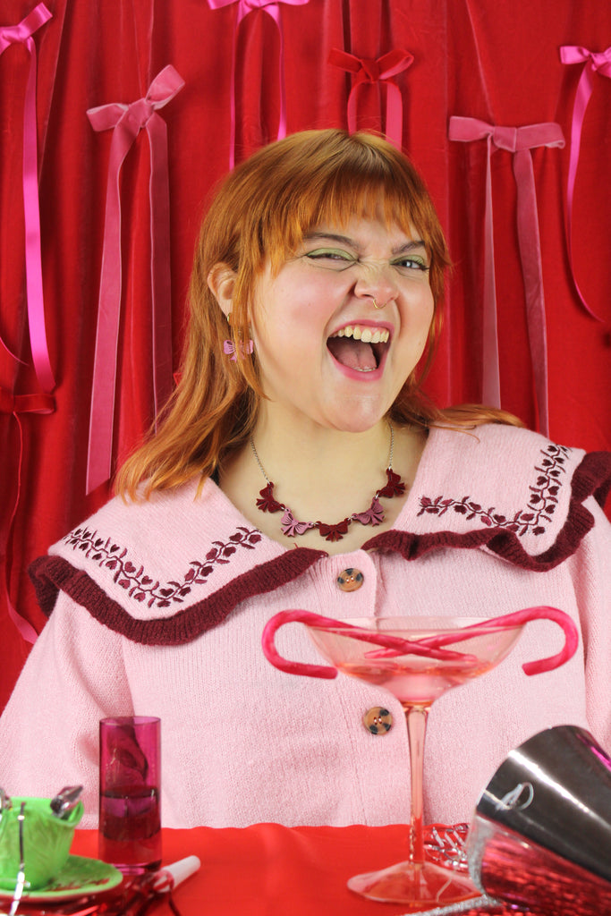 Woman in a pink outfit with a martini glass against a red curtain background