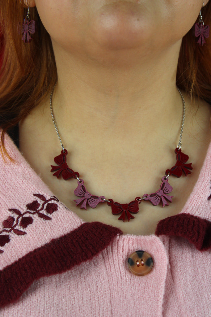 Necklace with red and pink bow pendants worn by a person.