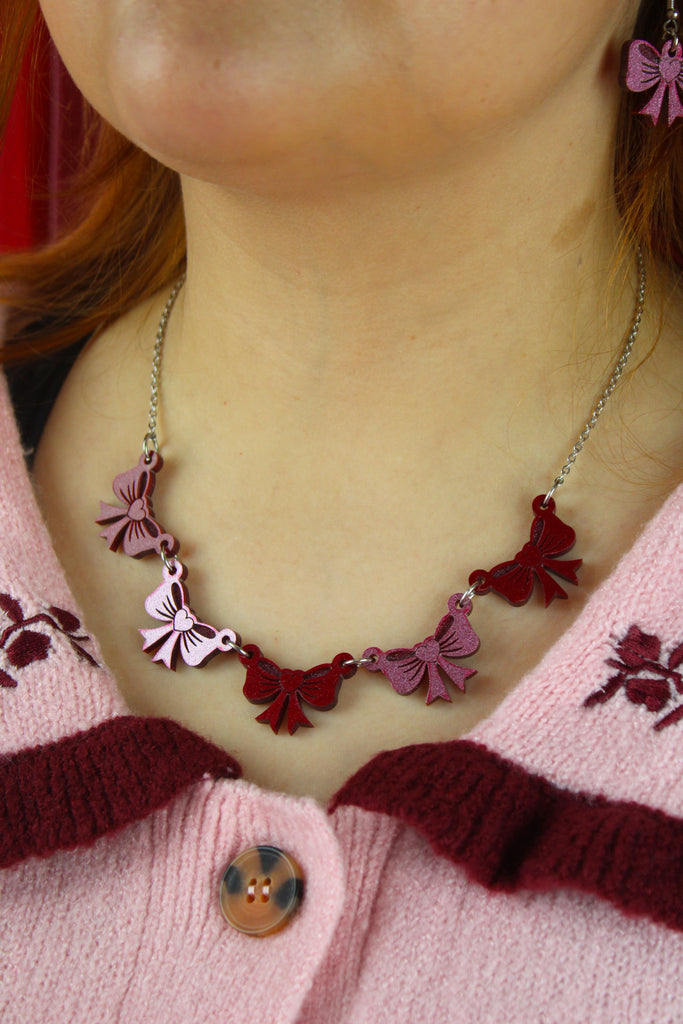 Necklace with bow pendants worn by a person in a pink garment.
