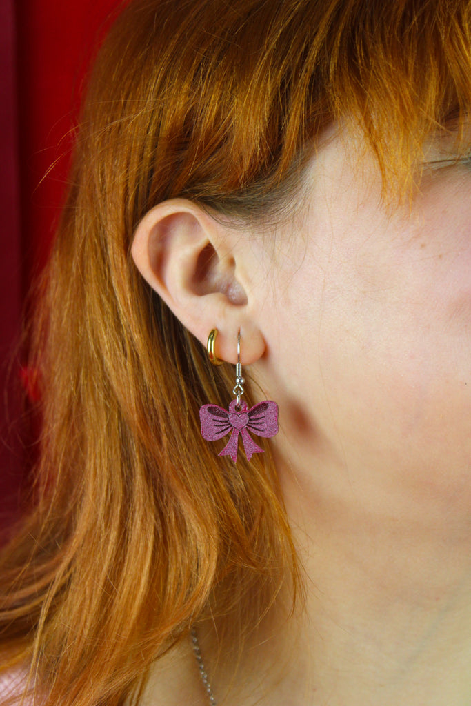 Close-up of a person wearing pink bow-shaped earrings with a red background