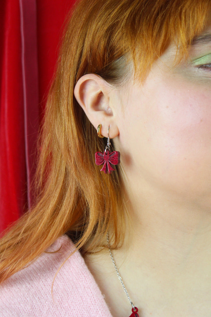 Close-up of a person wearing red bow earrings with a red curtain background