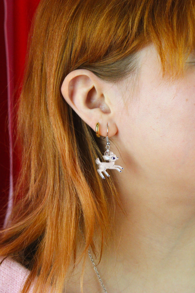 Close-up of a person wearing a fawn shaped earring with a red background